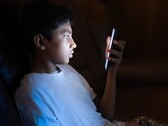 Un adolescente in una stanza buia che guarda uno smartphone illuminato
