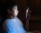 Un adolescente in una stanza buia che guarda uno smartphone illuminato