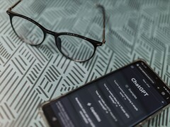 Smartphone con l’app ChatGPT aperta accanto a un paio di occhiali su una superficie a motivi