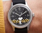 Primo piano del quadrante nero del Timex MK1 che raffigura Snoopy su uno sfondo a scacchi gialli e neri con indici arabi e lancette luminescenti.