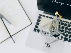 Carrello della spesa in miniatura sulla tastiera di un laptop, con la scritta «Acquista ora» sullo schermo