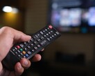 Mano che tiene un telecomando con una TV sfocata sullo sfondo