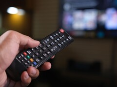 Mano che tiene un telecomando con una TV sfocata sullo sfondo