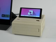 Un mini PC Ayaneo AM01S in stile retrò con finitura beige, dotato di un display secondario flip-up integrato che mostra il desktop di Windows. (ETA Prime via YouTube)