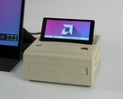 Un mini PC Ayaneo AM01S in stile retrò con finitura beige, dotato di un display secondario flip-up integrato che mostra il desktop di Windows. (ETA Prime via YouTube)