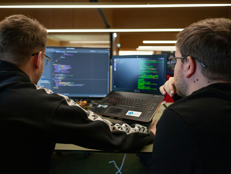 I ricercatori analizzano il codice su due monitor (Fonte: Flipsnack / Unsplash)