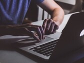 Mani che digitano sulla tastiera di un MacBook in condizioni di scarsa illuminazione, con il logo Apple che risplende