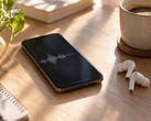 Smartphone che mostra una forma d'onda audio accanto ad auricolari wireless e a una tazza di caffè su una scrivania in legno