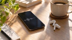 Smartphone che mostra una forma d'onda audio accanto ad auricolari wireless e a una tazza di caffè su una scrivania in legno