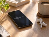 Smartphone che mostra una forma d'onda audio accanto ad auricolari wireless e a una tazza di caffè su una scrivania in legno
