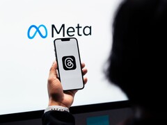 Una mano tiene uno smartphone davanti a un grande logo Meta