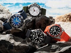 Quattro orologi subacquei Citizen Promaster Marine nei colori bianco, nero, blu e arancione, esposti su alcune rocce in riva al mare.