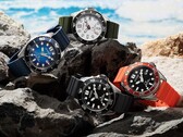 Quattro orologi subacquei Citizen Promaster Marine nei colori bianco, nero, blu e arancione, esposti su alcune rocce in riva al mare.