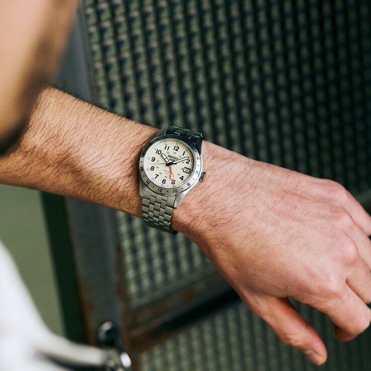 Vista frontale del Seiko 5 Sports Field GMT HDB002 con quadrante color crema, lancetta GMT arancione, lunetta fissa da 24 ore e bracciale in acciaio inossidabile.