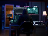 Un ricercatore incappucciato lavora su più schermi in un ambiente buio. Nella foto un hacker generico. 