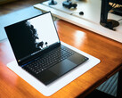 Un laptop da gaming Razer Blade 16 nero opaco, con lo schermo aperto, appoggiato su un tappetino da scrivania bianco posto su un tavolo in legno dai toni caldi, su cui è visualizzato uno sfondo in bianco e nero dai colori vivaci.