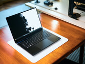 Un laptop da gaming Razer Blade 16 nero opaco, con lo schermo aperto, appoggiato su un tappetino da scrivania bianco posto su un tavolo in legno dai toni caldi, su cui è visualizzato uno sfondo in bianco e nero dai colori vivaci.