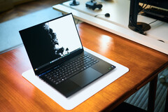 Un laptop da gaming Razer Blade 16 nero opaco, con lo schermo aperto, appoggiato su un tappetino da scrivania bianco posto su un tavolo in legno dai toni caldi, su cui è visualizzato uno sfondo in bianco e nero dai colori vivaci.