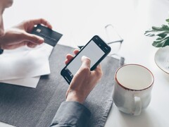 Persona che digita su uno smartphone mentre tiene una carta di credito nell’altra mano