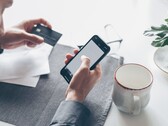 Persona che digita su uno smartphone mentre tiene una carta di credito nell’altra mano