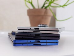 Pila di smartphone pieghevoli che rappresentano il concetto del prossimo Apple iPhone Fold, posizionati su un tavolo bianco con una pianta in vaso sullo sfondo (Fonte: Notebookcheck)