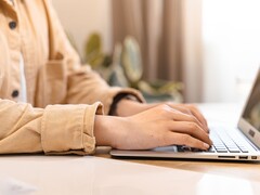 Mani che digitano sulla tastiera di un laptop aperto su una scrivania illuminata