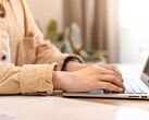 Mani che digitano sulla tastiera di un laptop aperto su una scrivania illuminata