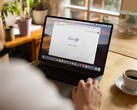 Persona davanti a un laptop con la homepage di Google aperta, accanto a una tazza di caffè