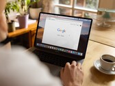 Persona davanti a un laptop con la homepage di Google aperta, accanto a una tazza di caffè