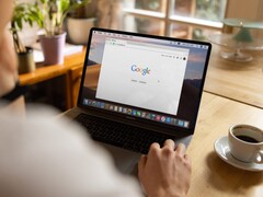 Persona davanti a un laptop con la homepage di Google aperta, accanto a una tazza di caffè