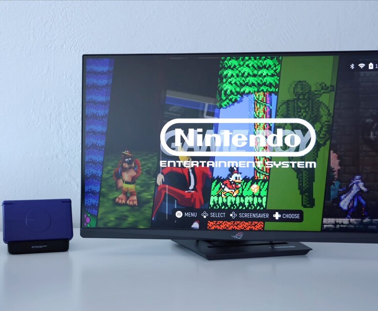 Retroid Pocket Flip 2 in viola posizionato su un dock accanto a un monitor, con lo schermo TV che mostra un'interfaccia di emulatore NES retrò. (Fonte immagine: Retro Game Corps su YouTube)