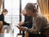Un'adolescente guarda il suo smartphone, mentre sullo sfondo due adulti siedono fuori fuoco.