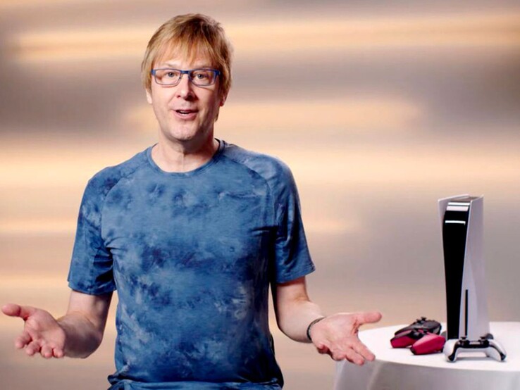 Mark Cerny durante un evento PlayStation, seduto accanto a una console PS5 e ai controller DualSense. (Fonte immagine: Sony Interactive Entertainment)