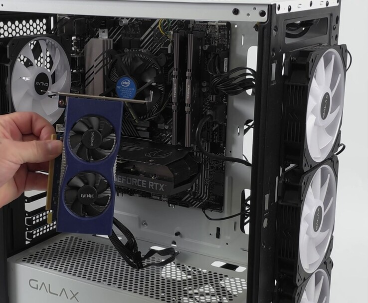 Una mano che tiene una scheda grafica Intel Arc A380 accanto a un PC con una Nvidia GeForce RTX 3060, preparata per una configurazione dual-GPU con Lossless Scaling (Fonte immagine: ETA PRIME via YouTube)
