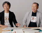 Uno screenshot di Shigru Miyamoto e Tezuka Takashi che indossano le magliette del 30° anniversario di Super Mario Bros