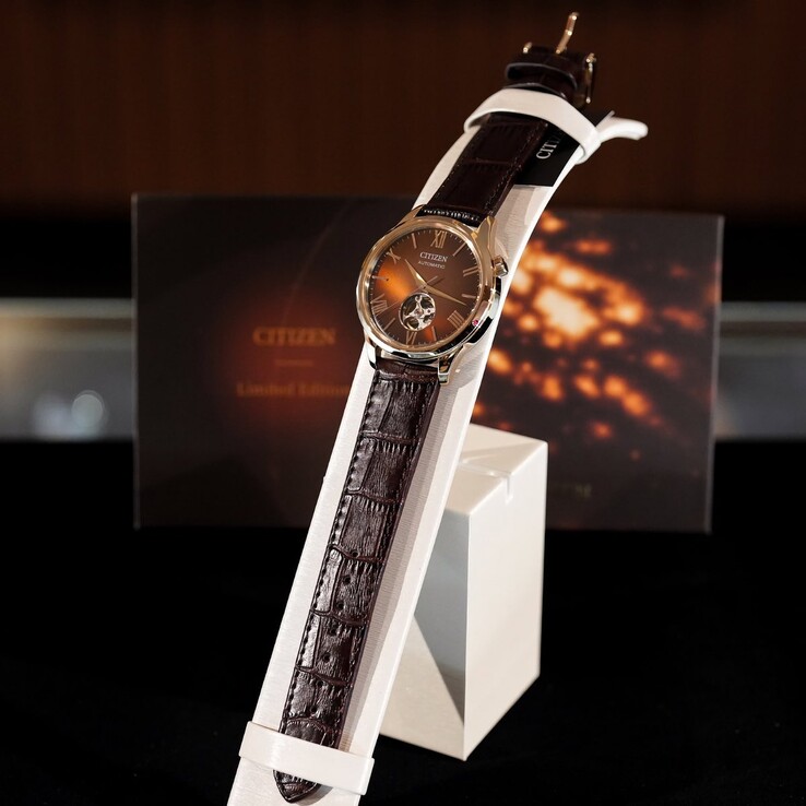 L'orologio Citizen è posizionato su un espositore bianco e curvo. L'immagine mostra l'intera lunghezza del cinturino in pelle marrone scuro con goffratura a pelle di coccodrillo e il quadrante marrone riflettente,