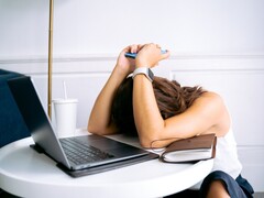 Donna che guarda il proprio smartphone con un computer portatile accanto a sé