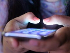 Due mani tengono uno smartphone con lo schermo luminoso nella penombra