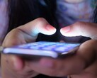 Due mani tengono uno smartphone con lo schermo luminoso nella penombra