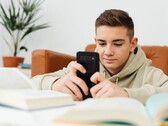 Adolescente con una felpa con cappuccio che digita su uno smartphone con i libri di scuola aperti davanti a sé