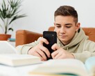 Adolescente con una felpa con cappuccio che digita su uno smartphone con i libri di scuola aperti davanti a sé