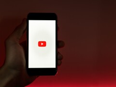 Una mano che regge uno smartphone con il logo di YouTube illuminato sul display su uno sfondo rosso
