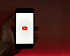 Una mano che regge uno smartphone con il logo di YouTube illuminato sul display su uno sfondo rosso