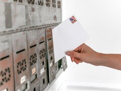 Una mano che inserisce una busta in una fila di cassette postali