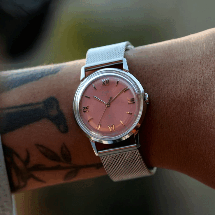 Persona che indossa l’orologio Timex x Todd Snyder Marlin Mesh con quadrante color salmone effetto sunburst e bracciale a maglia.