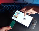 Yu del canale YouTube Better Gaming tiene in una mano un Nintendo Switch 2 e nell'altra un adattatore PCB verde open-source, cercando di inserirlo nello slot microSD Express del dispositivo (Fonte immagine: Better Gaming via YouTube)