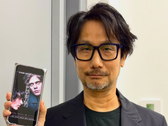 Hideo Kojima mostra un poster di Physint sul suo telefono