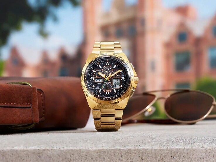 Orologio da pilota Citizen Promaster Skyhawk A-T JY8144-50E color oro, esposto in posizione verticale su una mensola accanto a una borsa in pelle marrone e a un paio di occhiali da sole, con uno scorcio sfocato della città sullo sfondo.
