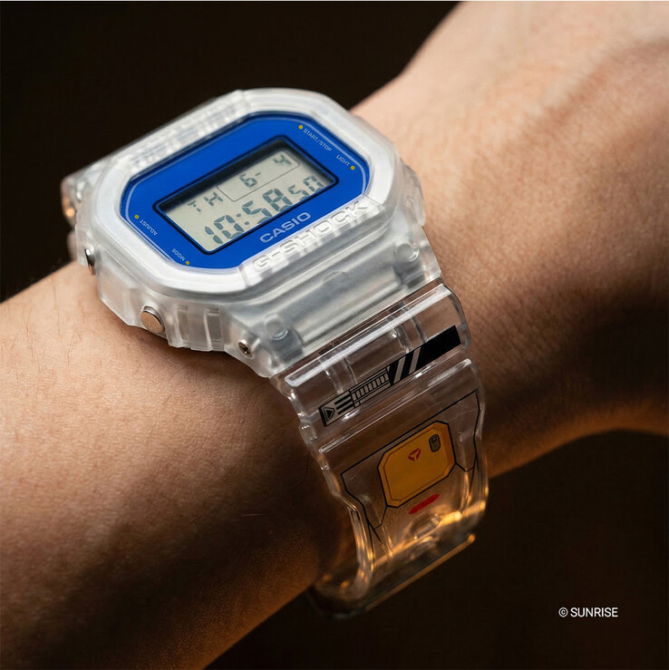 Casio G-Shock x Mobile Suit Gundam DW-5600GM26-7DR indossato al polso, con cassa e cinturino in resina trasparente, cornice blu della lunetta e grafica ispirata a Gundam sul cinturino.