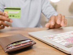 Persona che tiene una carta bancaria davanti a un laptop, con un portafoglio sulla scrivania